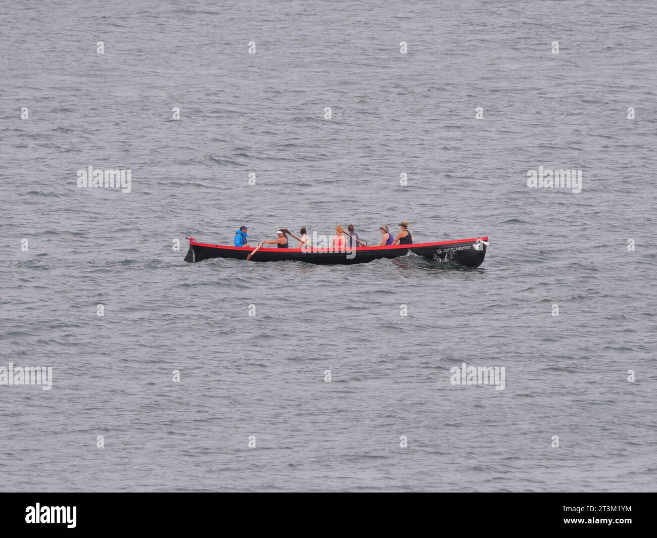 Sieben Leute sitzen in einem roten Ruderboot und rudern über das Meer Stockfoto
