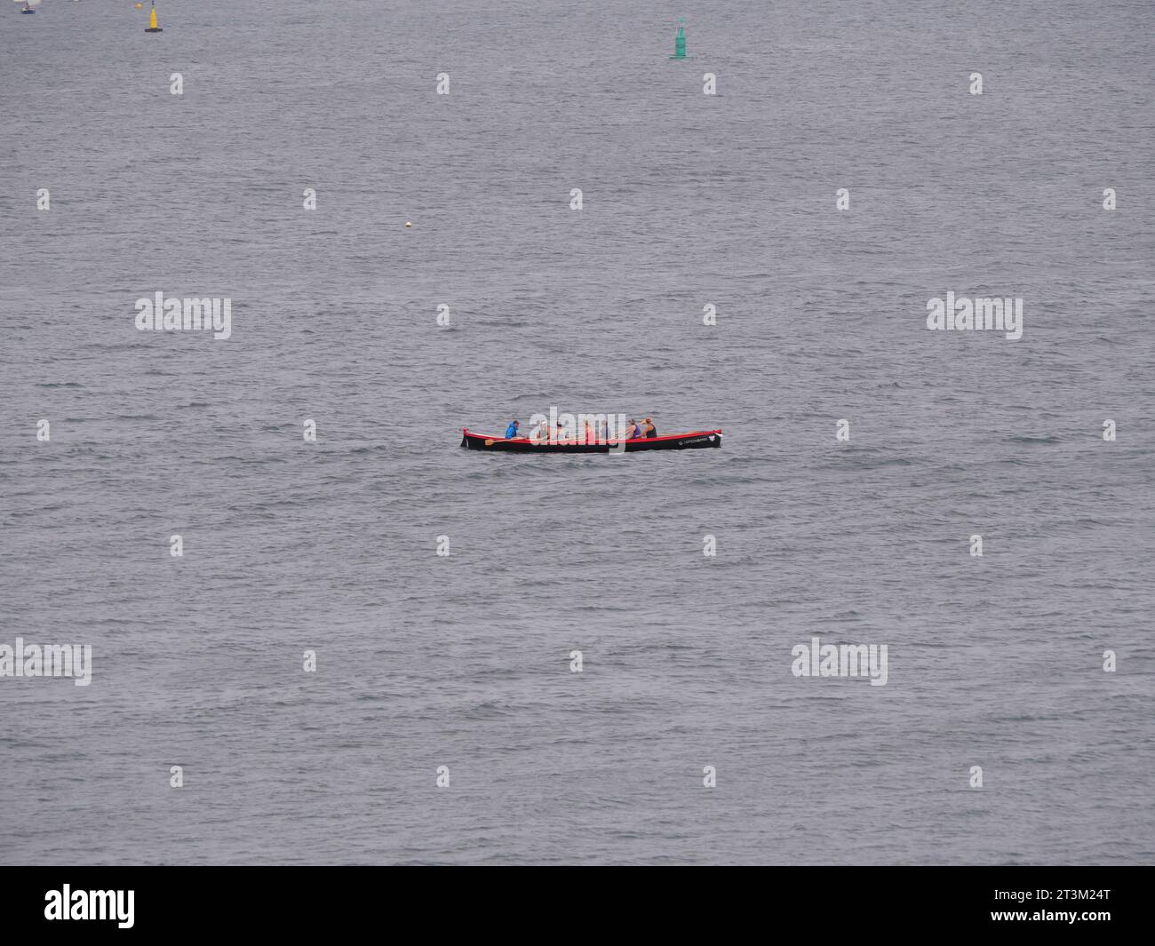 Sieben Leute sitzen in einem roten Ruderboot und rudern über das Meer Stockfoto