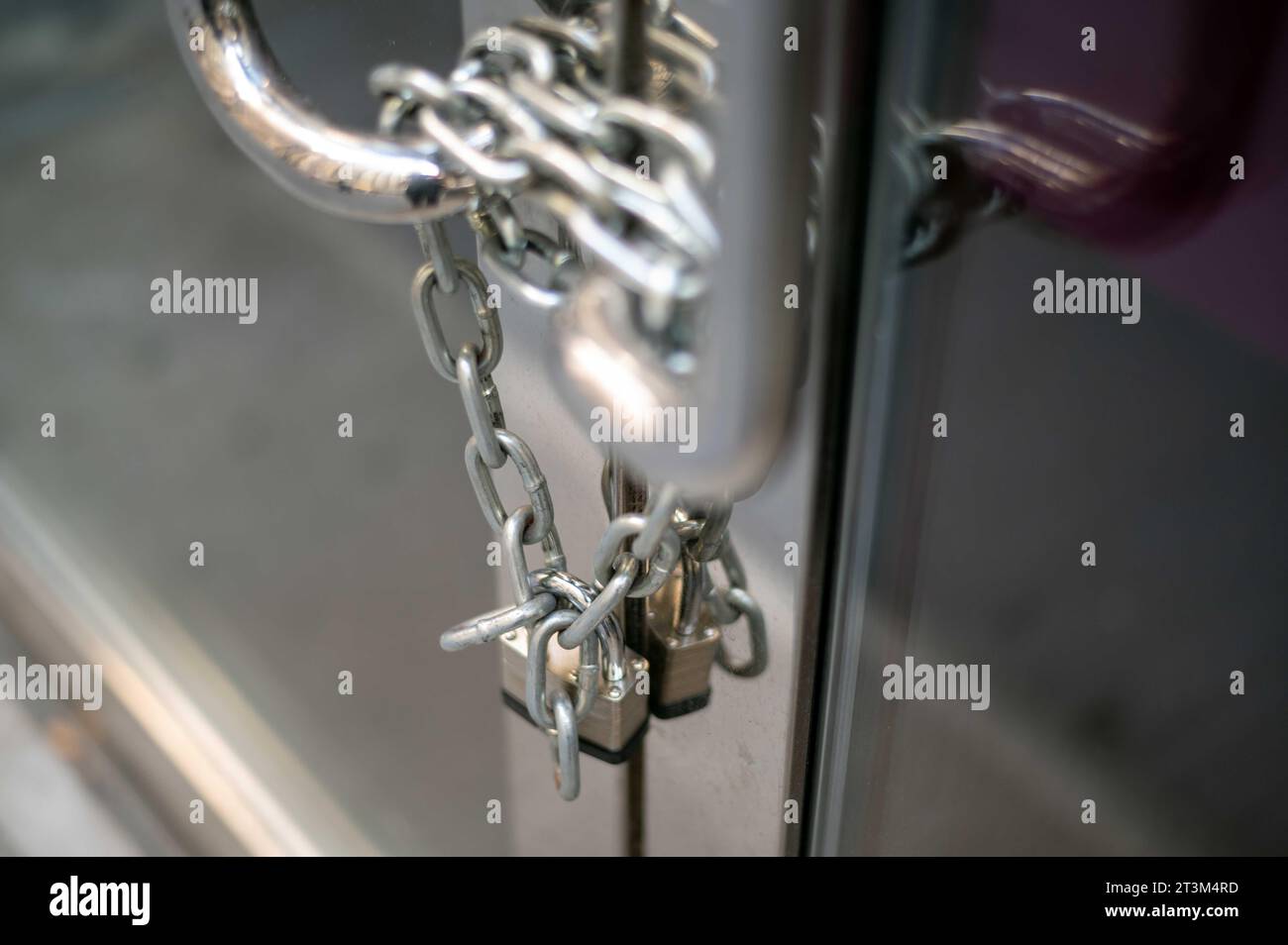 Kette und Vorhängeschloss an geschlossener Business-Glastür mit Metallgriffen Stockfoto