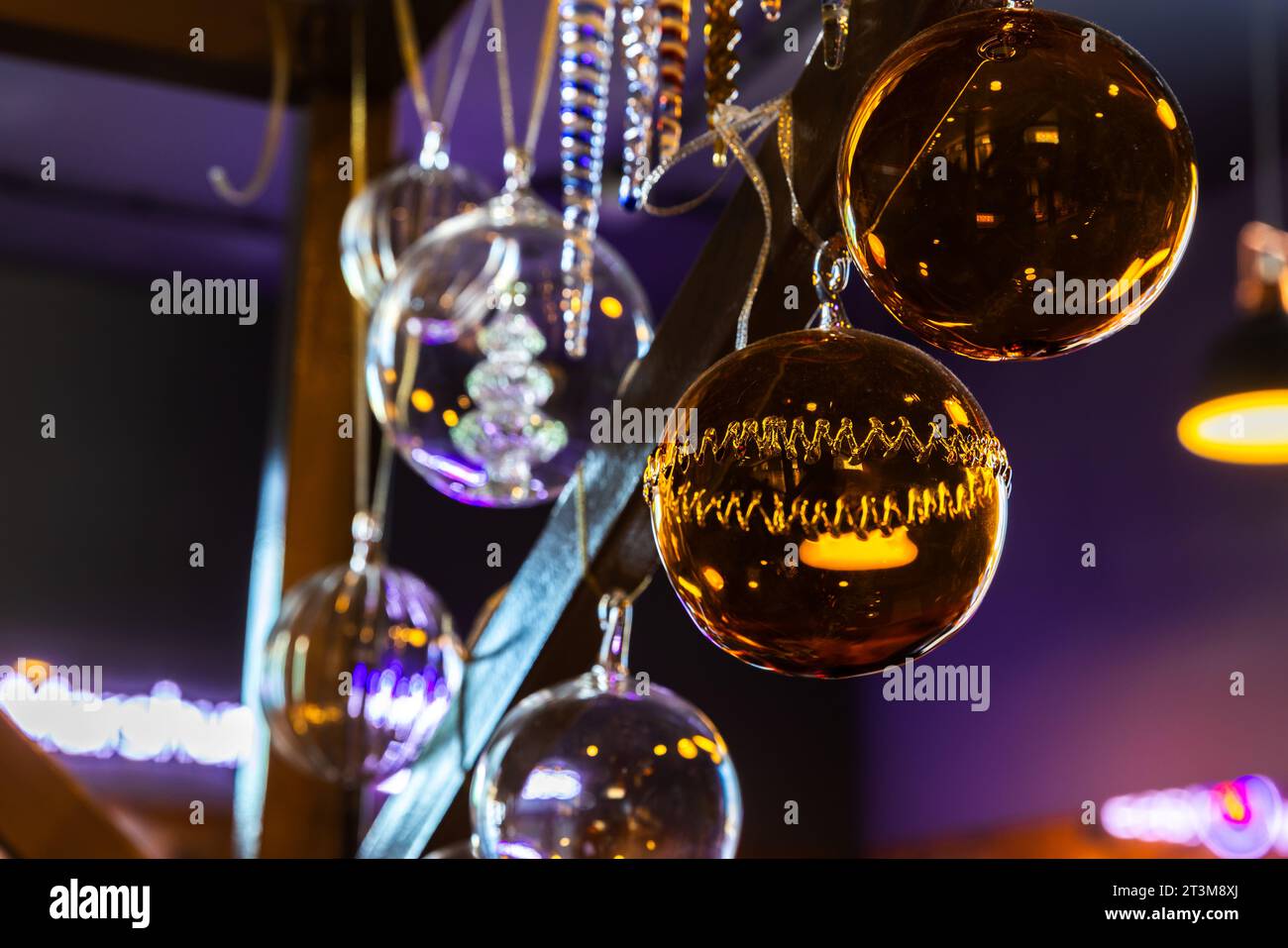 Weihnachtsdekoration hängt in einem dunklen Innenraum, farbenfrohe transparente Glaskugeln Stockfoto
