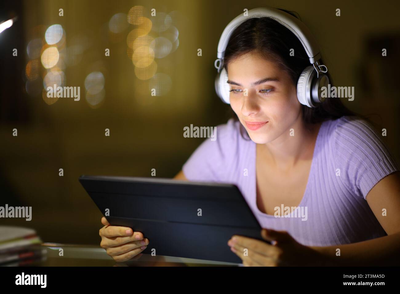 Frau in der Nacht, die zu Hause Kopfhörer und Tablet verwendet Stockfoto