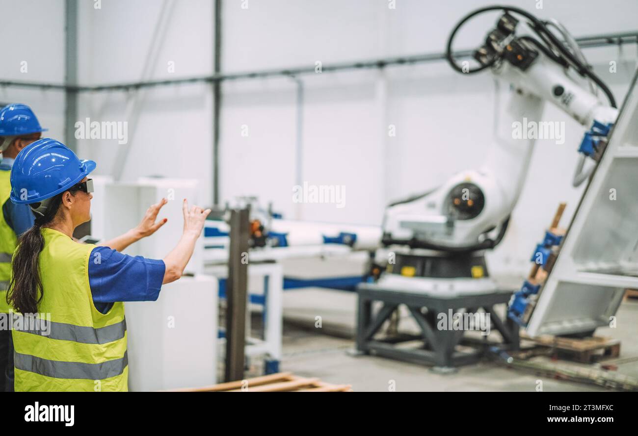 Arbeitnehmerin mit futuristischer Augmented-Reality-Brille in einer Roboterfabrik bei der Arbeit mit KI-Maschinen – Industrie- und Technologiekonzept – F Stockfoto
