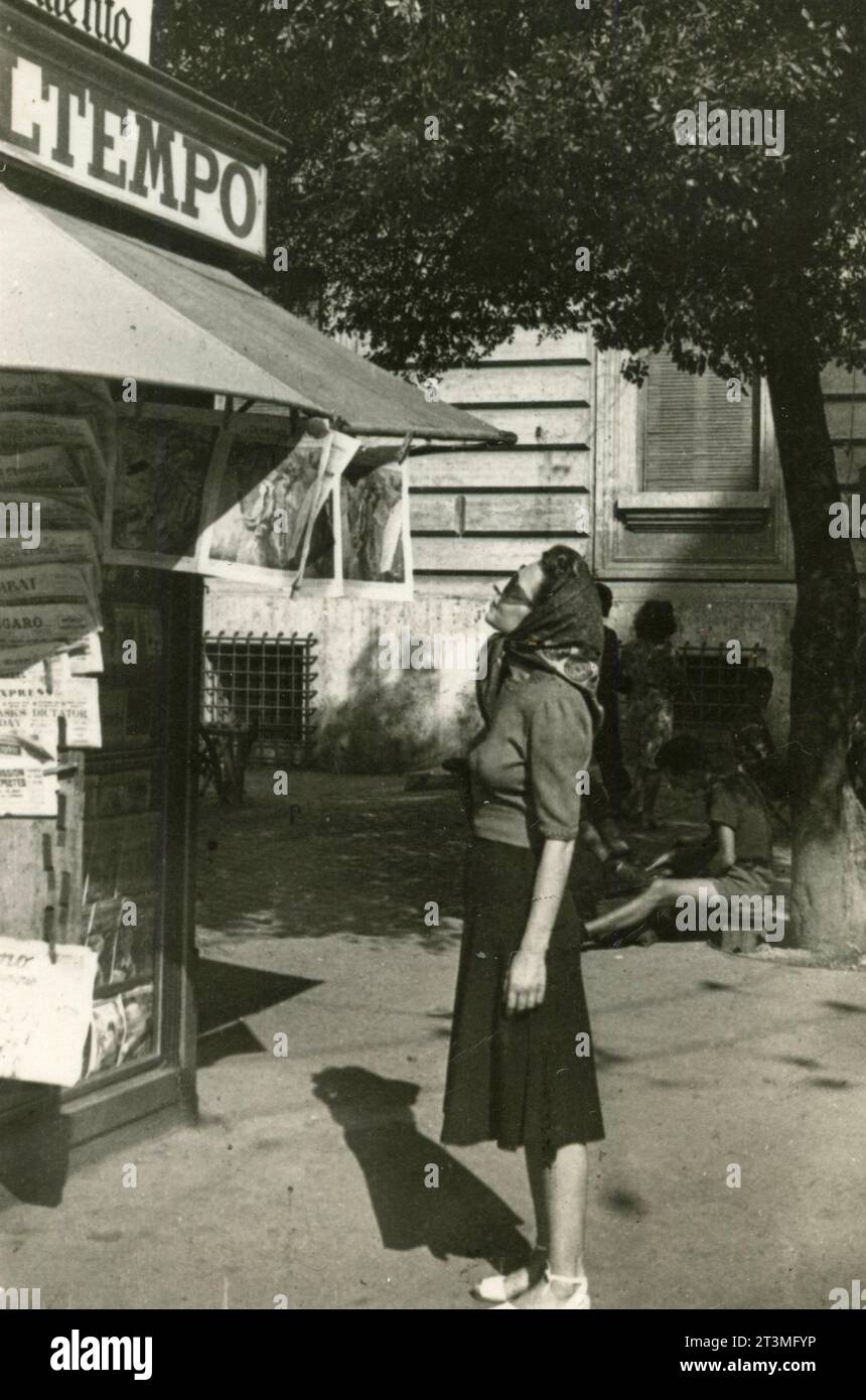 Frau mit Kopftuch, die in einen Zeitungskiosk schaut, Italien 1947 Stockfoto