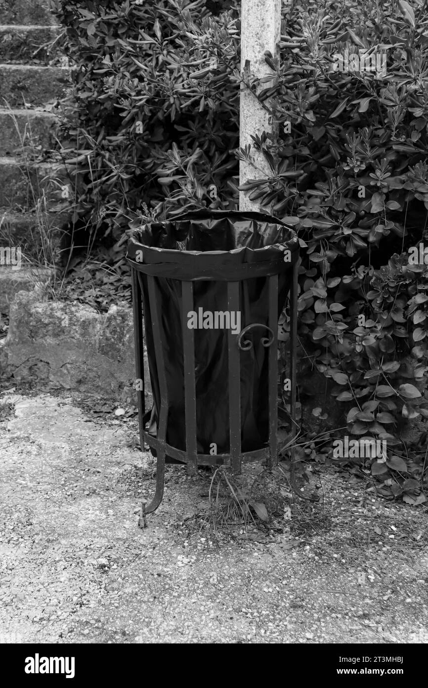Metallmüllbehälter für den Außenbereich mit Plastiktüte an der Akropolis von Rhodos zur öffentlichen Verwendung in Schwarz-weiß Stockfoto