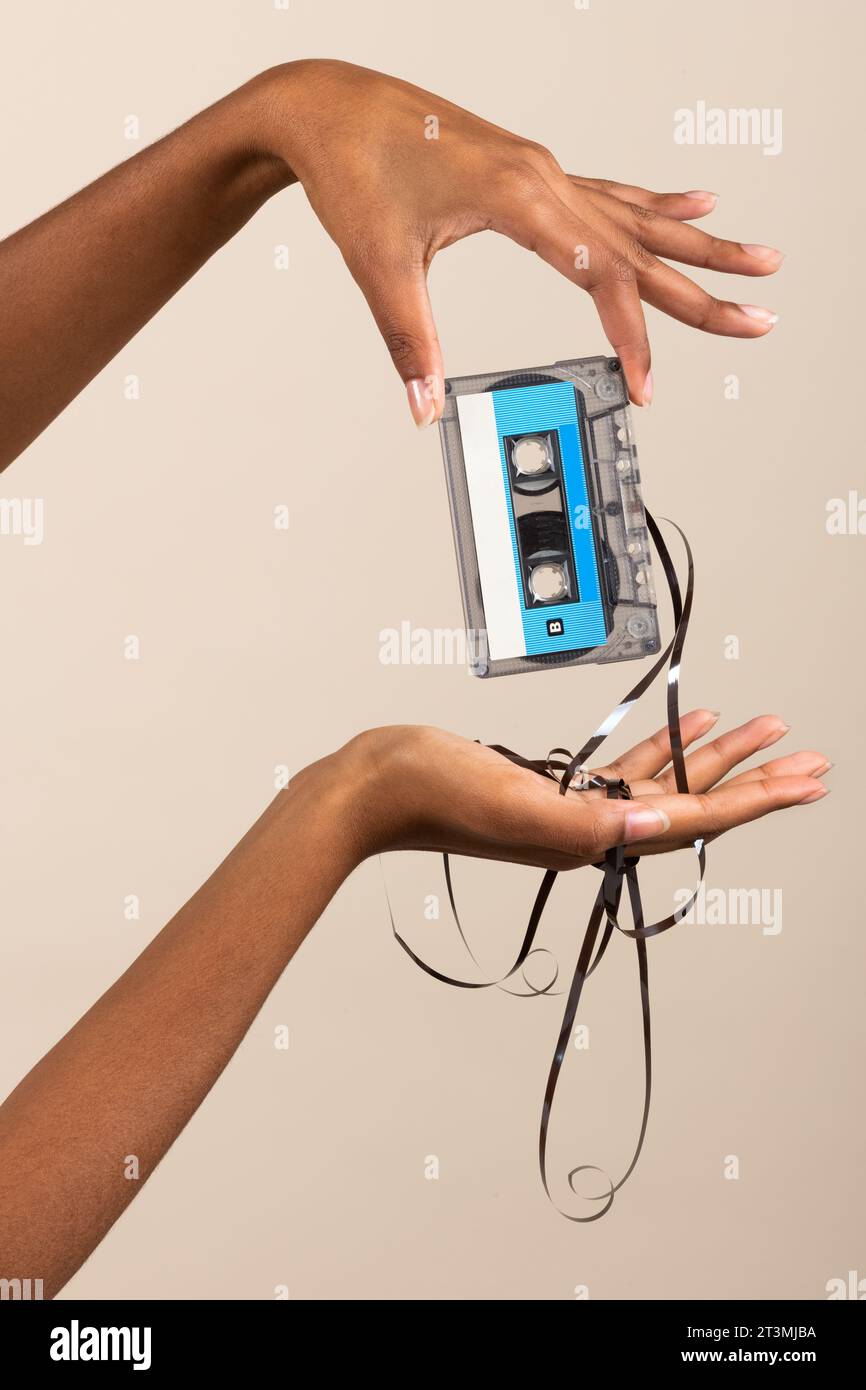 Seitenansicht einer anonymen jungen ethnischen Frau, während sie im Zimmer stand und eine Vintage-Kassette mit ausgelaufenem Klebeband in gepflegten Fingerhänden A vorführte Stockfoto