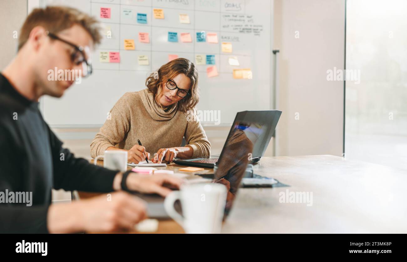 Geschäftsleute und Geschäftsfrauen arbeiten gemeinsam an einem Projekt in einem kreativen Büro. Das Team, einschließlich eines Scrum-Masters, konzentriert sich auf Software Stockfoto