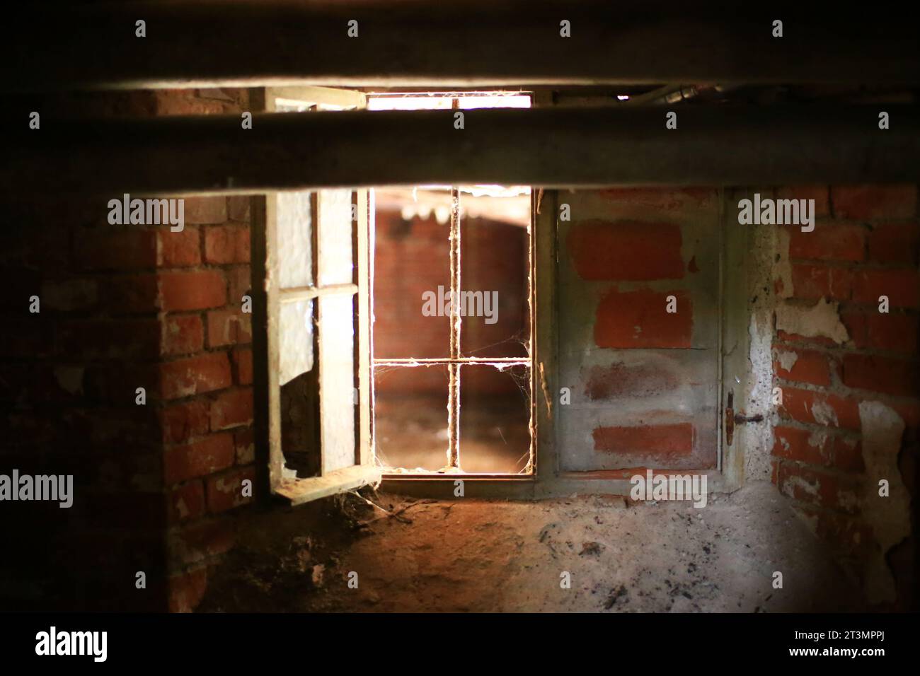 Das Fenster im Keller war von Mauern umgeben, die Scheiben waren kaputt und es fiel etwas Tageslicht herein. Stockfoto
