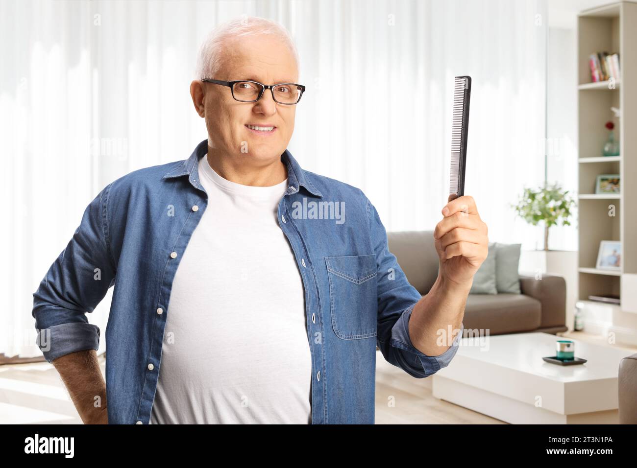 Reifer Mann mit weißem Haar, der zu Hause im Wohnzimmer einen Haarkamm hält Stockfoto