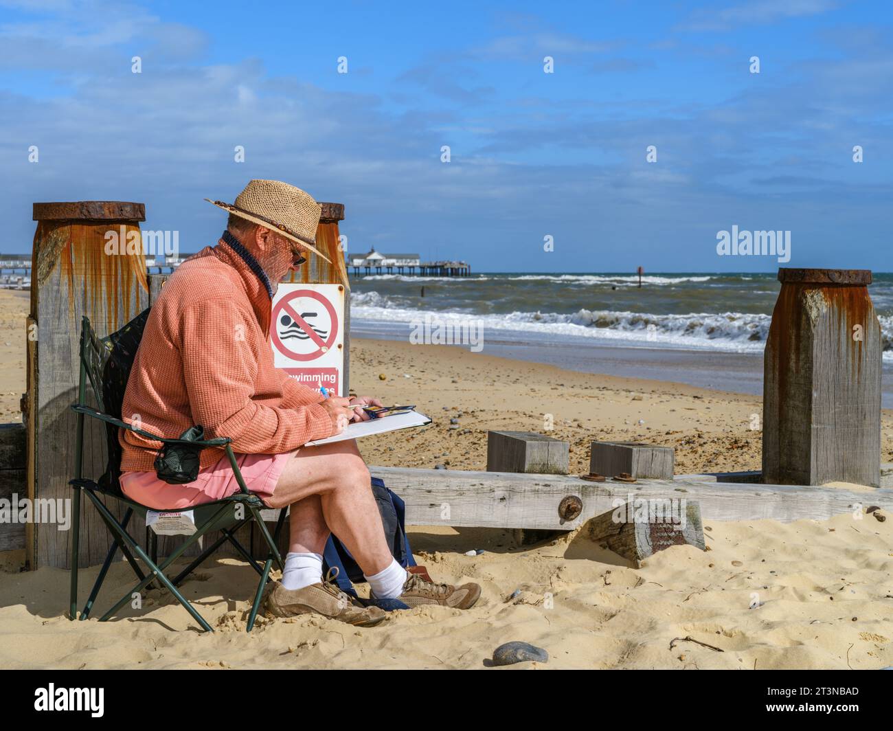 An einem warmen Sommertag sitzt ein Mann geduldig und malt die Meereslandschaft am Strand von Southwold in Suffolk, England. Stockfoto