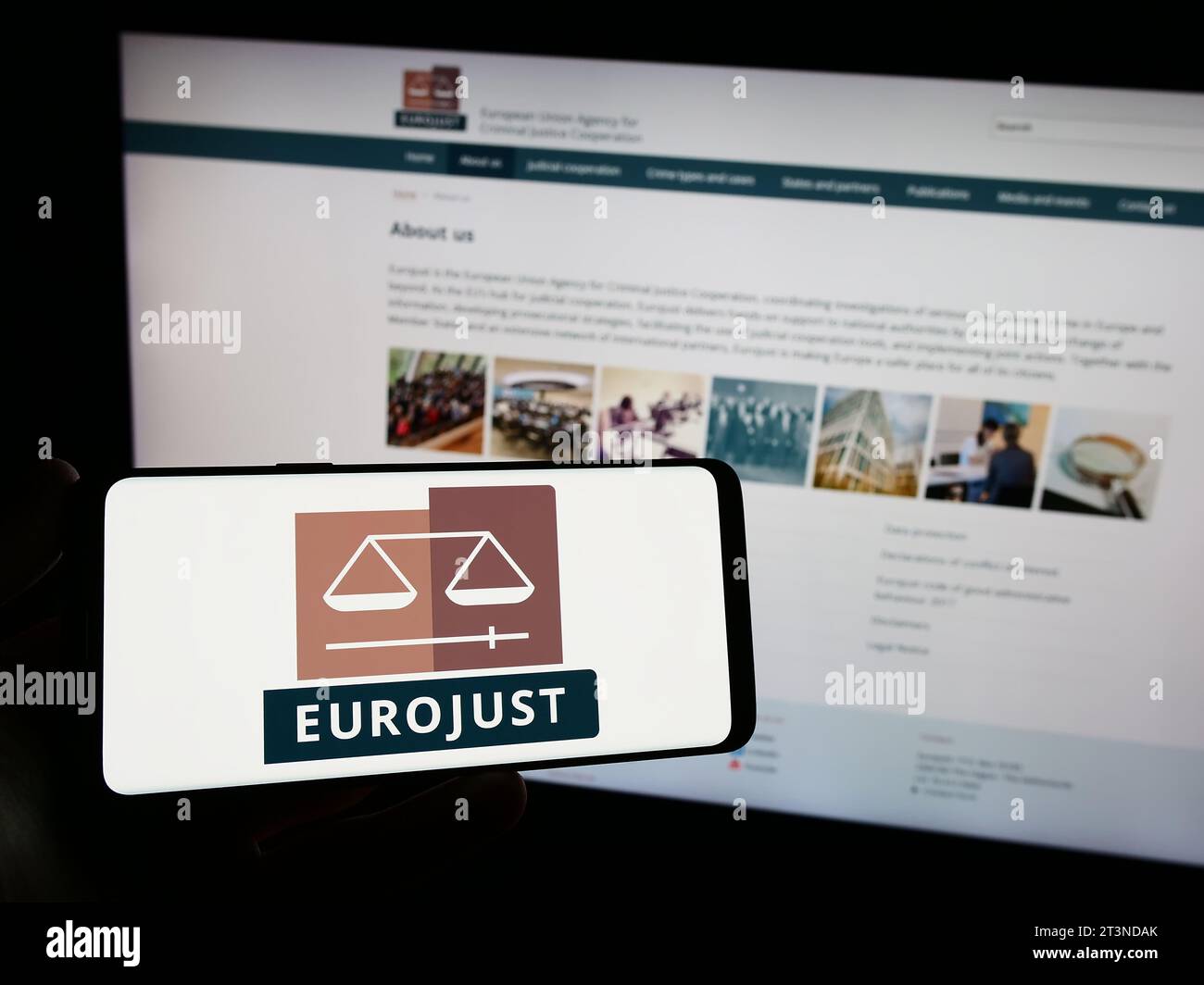 Person mit Smartphone und Logo der EU-Agentur für justizielle Zusammenarbeit in Strafsachen (Eurojust) vor der Website. Schwerpunkt auf dem Display des Telefons. Stockfoto