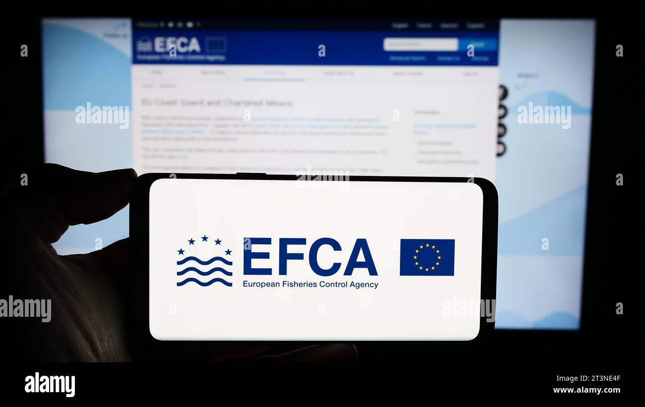 Person, die ein Mobiltelefon mit dem Logo der Europäischen Fischereiaufsichtsagentur (EFCA) des EU-Organs vor der Webseite hält. Schwerpunkt auf dem Display des Telefons. Stockfoto