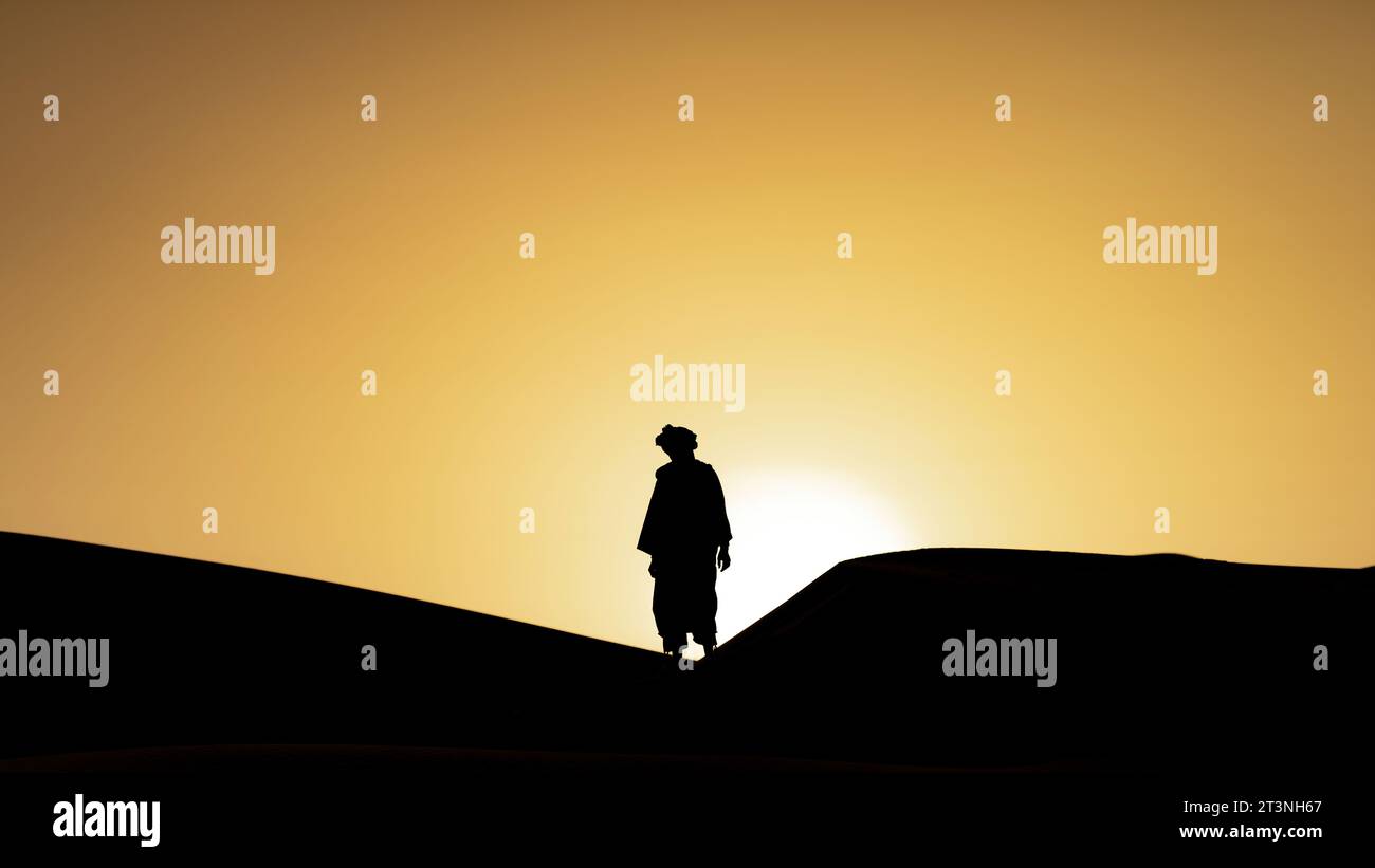 Silhouette eines nicht identifizierten Berbermanns in seiner traditionellen Kleidung, ein langes Gewand auf Sanddünen bei schönem Sonnenuntergang in der Sahara, Marokko Stockfoto