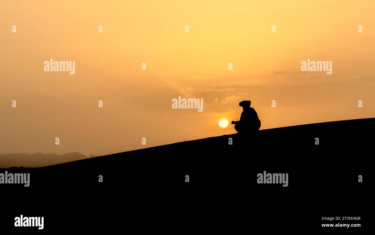 Silhouette eines nicht identifizierten Berbermanns, der den Sonnenuntergang auf Sanddünen bei einem wunderschönen Sonnenuntergang in der Sahara, Marokko, beobachtet Stockfoto
