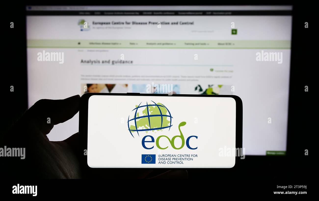 Person, die ein Mobiltelefon mit dem Logo des Europäischen Zentrums für die Prävention und die Kontrolle von Krankheiten (ECDC) vor der Webseite hält. Schwerpunkt auf dem Display des Telefons. Stockfoto