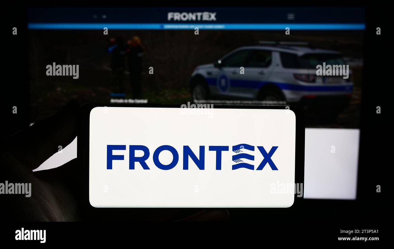 Person, die ein Smartphone mit dem Logo der Europäischen Agentur für die Grenz- und Küstenwache (Frontex) vor der Website hält. Schwerpunkt auf dem Display des Telefons. Stockfoto