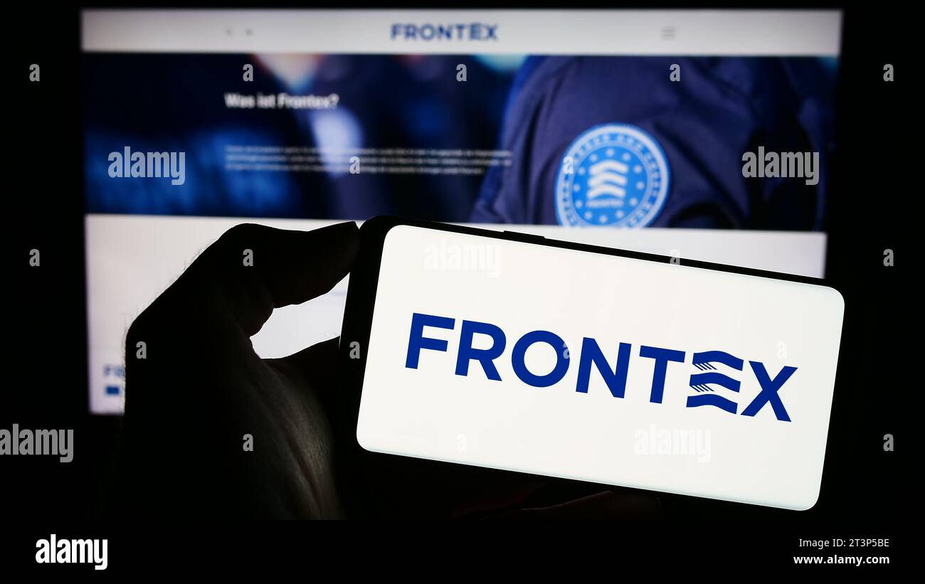 Person, die ein Mobiltelefon mit dem Logo der Europäischen Agentur für die Grenz- und Küstenwache (Frontex) vor der Webseite hält. Schwerpunkt auf dem Display des Telefons. Stockfoto