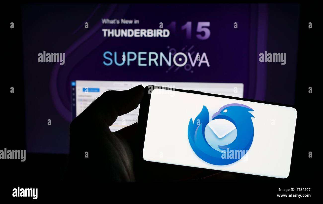 Person, die ein Mobiltelefon mit dem Logo des Open-Source-E-Mail-Clients Mozilla Thunderbird vor der Webseite hält. Schwerpunkt auf dem Display des Telefons. Stockfoto