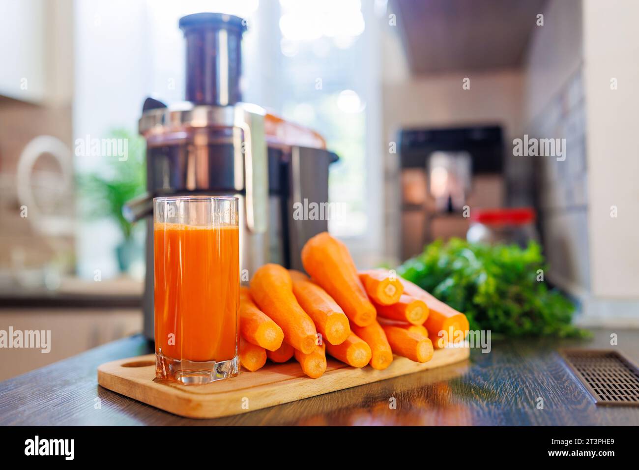 Ein Glas frisch gepressten Karottensaft, Karotten und Saftpresse in der Küche Stockfoto