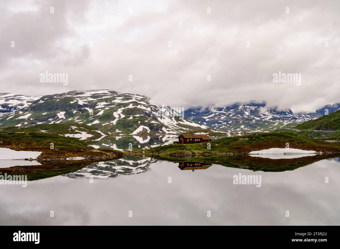 Berge mit Schnee und eine einsame Hütte, die sich in einem ruhigen See auf Haukelifjell in Norwegen spiegelt Stockfoto