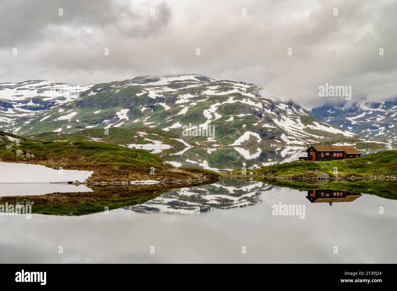 Berge mit Schnee und eine einsame Hütte, die sich in einem ruhigen See auf Haukelifjell in Norwegen spiegelt Stockfoto