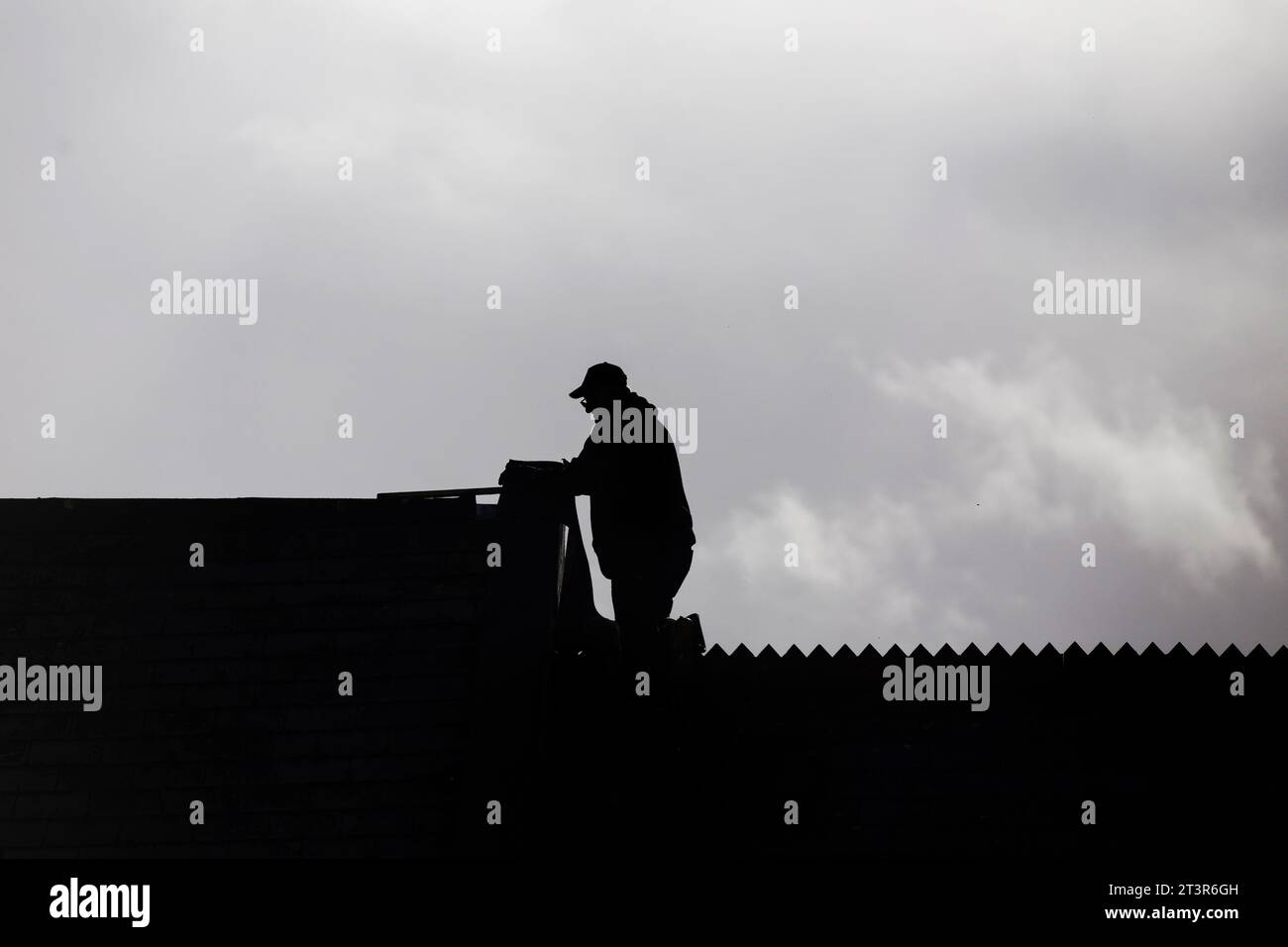 Schwarze Silhouette des Baumeisters (Dachdecker) auf einem Hausdach vor grauem, bewölktem Himmel Stockfoto