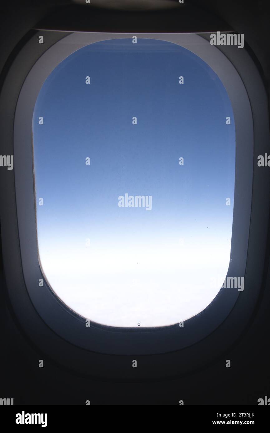 Nahaufnahme eines Fensters aus dem Inneren eines Flugzeugs, das den blauen Verlauf der oberen Atmosphäre zeigt Stockfoto