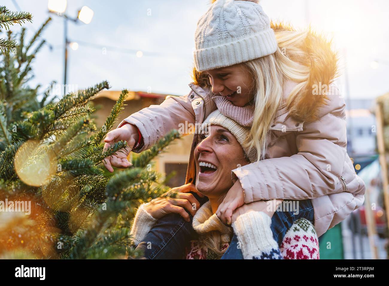 Beauty Winter Girl Blowing Snow auf ihrem ausgewählten Weihnachtsbaum auf einem Weihnachtsbaummarkt. Stockfoto