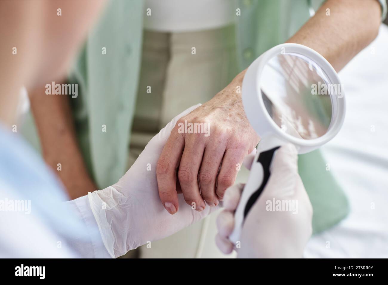 Nahaufnahme eines Arztes mit Lupe bei der Untersuchung der Hände einer Seniorin in der Dermatologischen Klinik, Kopierraum Stockfoto