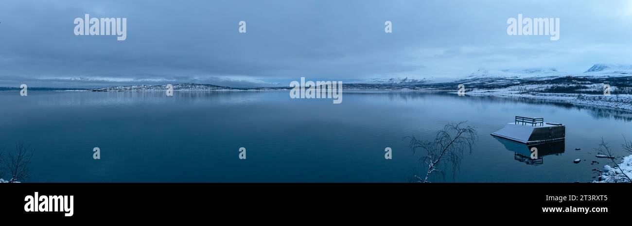 Panoramablick auf den Torneträsk See mit schneebedeckten Bergen unter einem dunklen bewölkten Himmel im Winter im Abisko Nationalpark Stockfoto