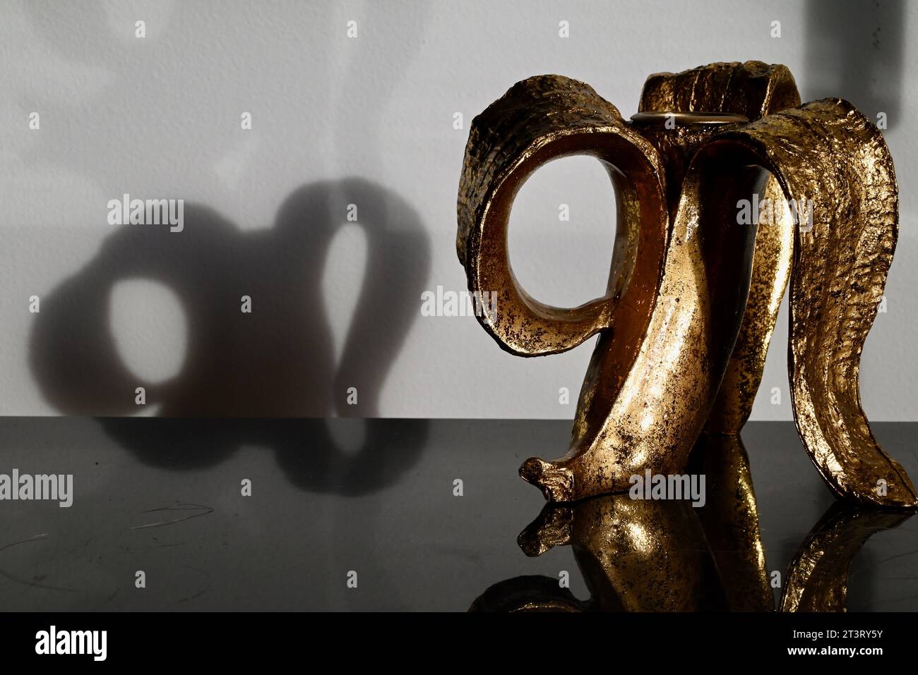 Bananenförmiger goldener Kerzenhalter, der in einem Metallschrank im Sonnenlicht reflektiert wird, das durch das Fenster kommt. Stockfoto