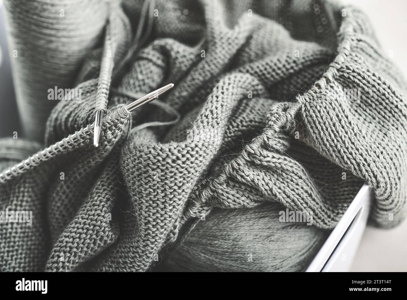 Projekt wird zusammengefügt. Ein Stück Stricken mit Garnknäueln und einer Stricknadeln Nahaufnahme Stockfoto
