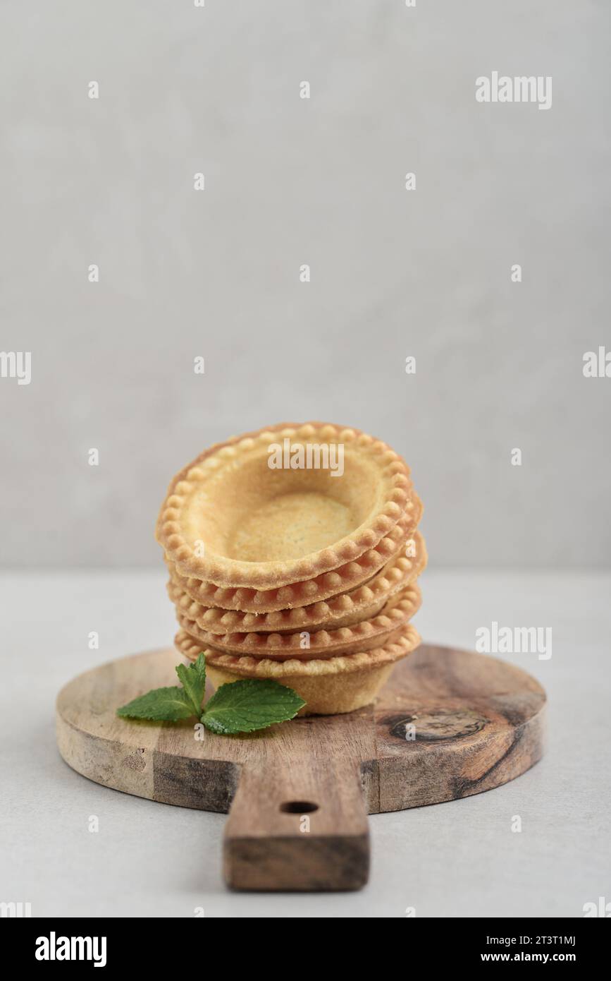 Leere Tartlet-Schalen auf hölzernem Schneidebrett auf hellem Hintergrund Stockfoto