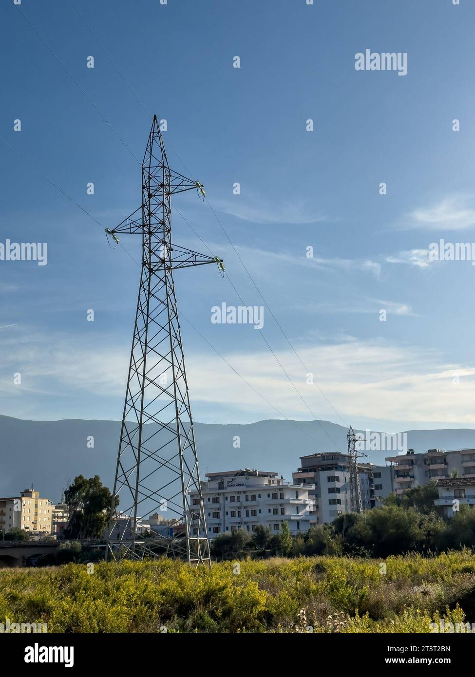 Freileitungsmasten, Hochspannungsmasten auf der Wiese mit Bergen im Hintergrund am sonnigen Sommertag, in der Nähe von Oricum, Albanien Stockfoto