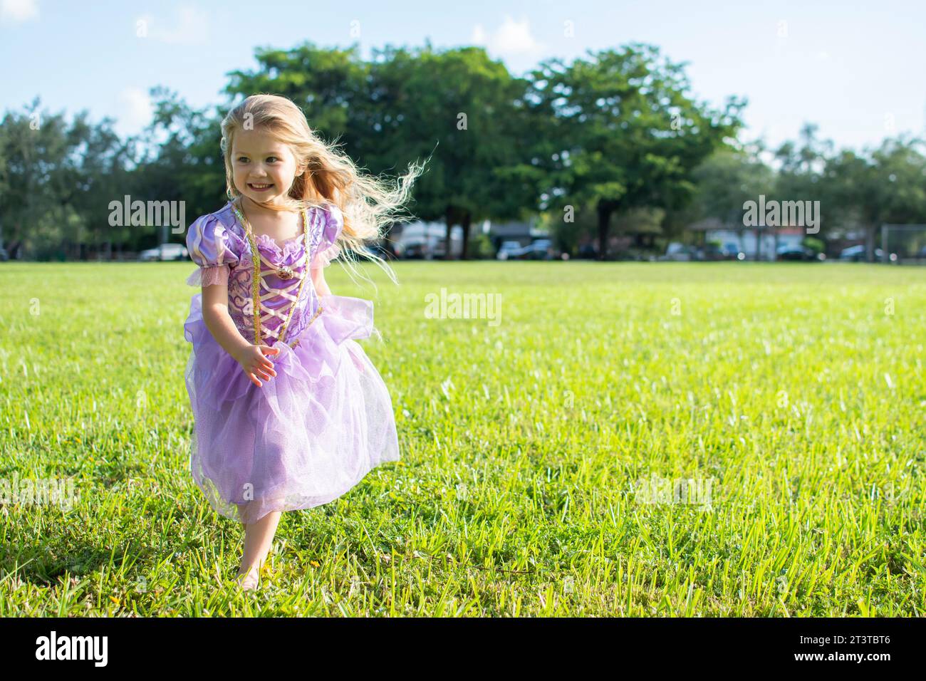 Ein kleines Mädchen mit langen blonden Haaren, das auf dem Feld läuft. Rapunzel Prinzessin, kleines Mädchen. Halloween-Kostüm, Halloween-Party Stockfoto