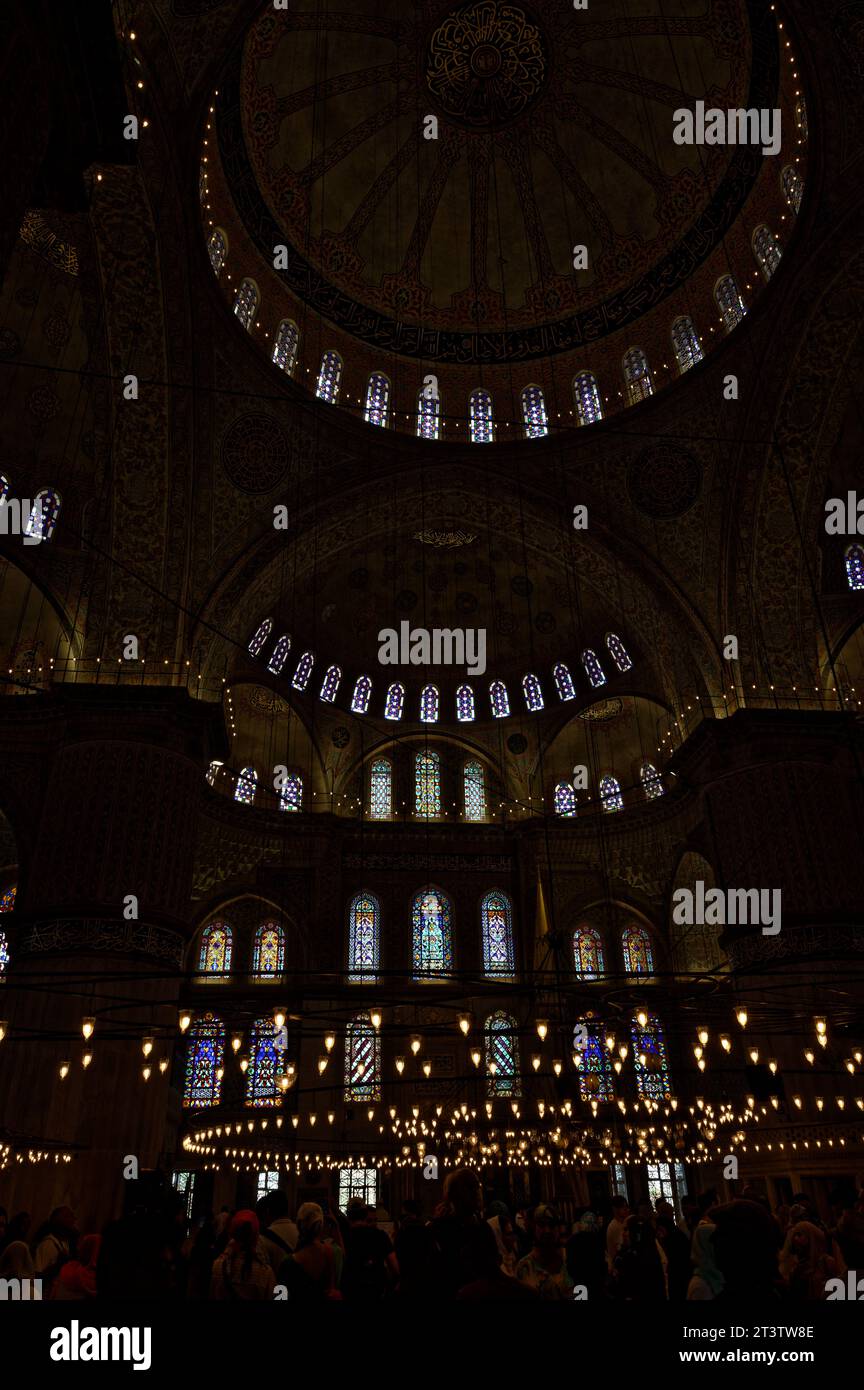 Im schwach beleuchteten Inneren der blauen Moschee entfaltet sich ein mystisches Ambiente, während ein Meer von Menschen interagiert. Stockfoto