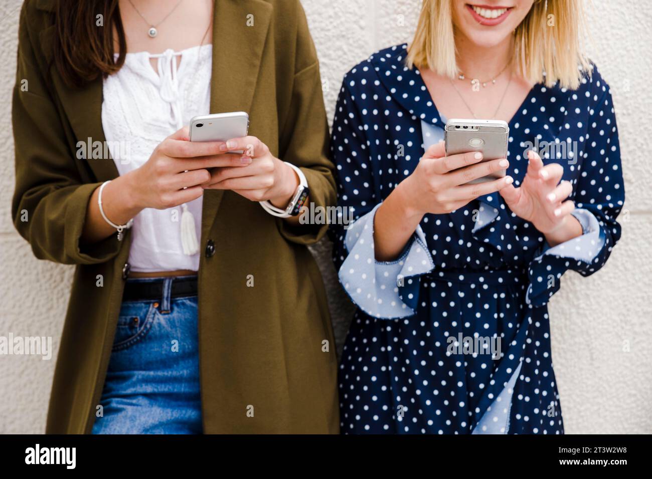 Weibliche Freunde, die sich mit dem Smartphone an die Wand lehnen Stockfoto