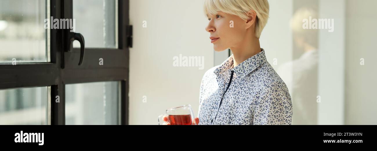 Eine rücksichtsvolle Frau mit Teetasse sieht aus dem Fenster im Büro Stockfoto