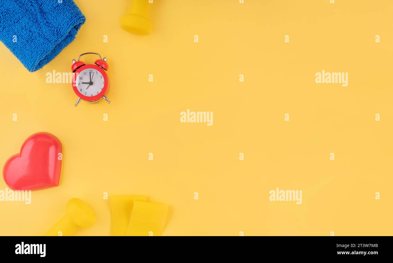 Neopren-Kurzhanteln, Fitness-Bänder elastisch, Herz, Mantel und Handtuch auf gelbem Hintergrund Top View, Flat Lay Fitness und gesundes Leben, Wellness-Konzept Stockfoto
