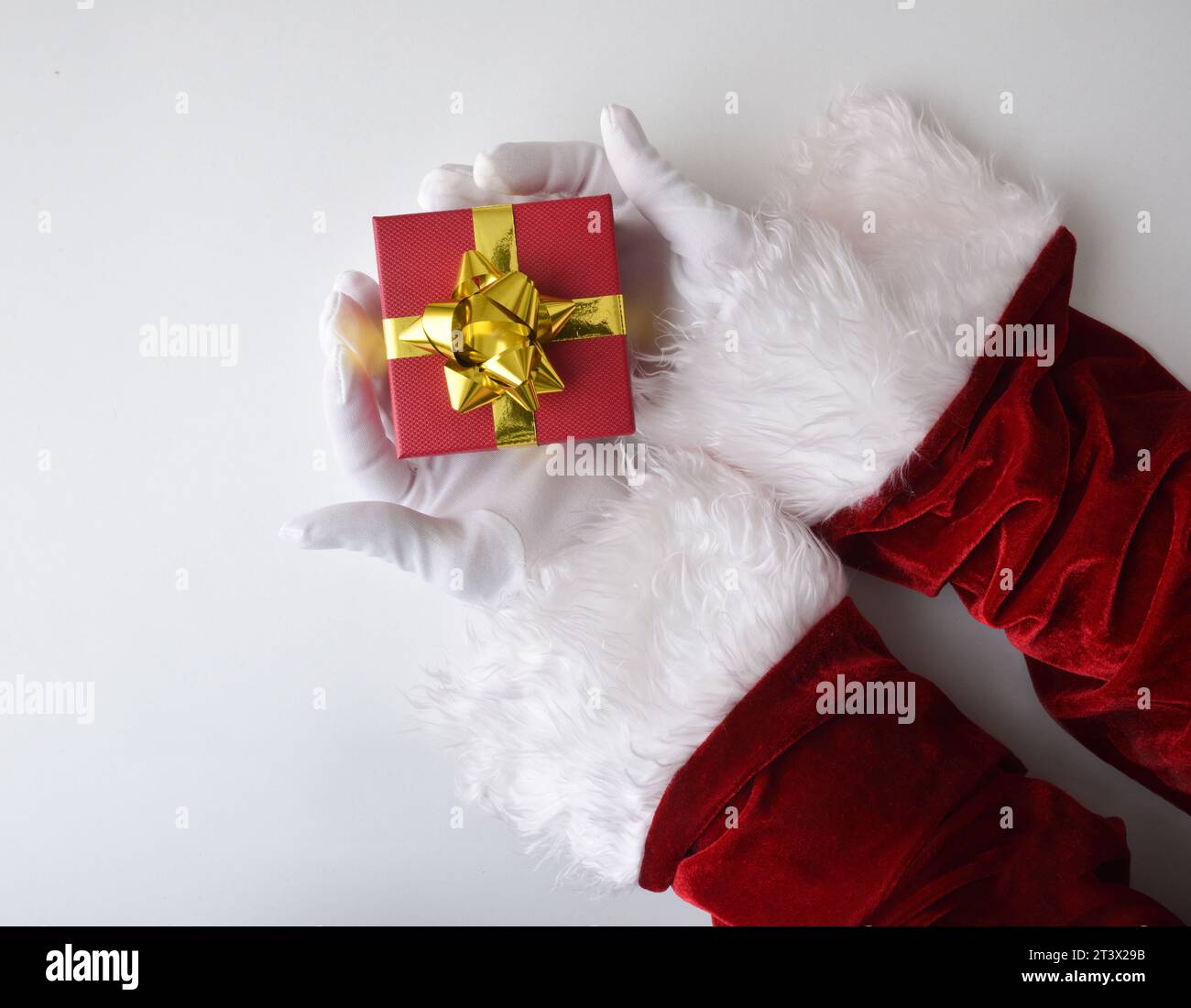 SaSanta Claus bietet ein Geschenk zwischen den Händen, gekleidet in seinem traditionellen roten Anzug mit weißen Handschuhen isoliert auf weißem Tisch. Draufsicht. Stockfoto