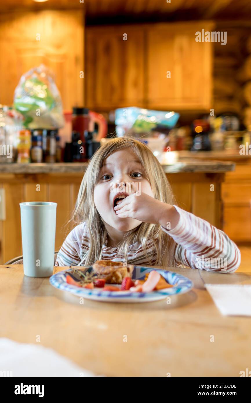 Glückliches Kleinkind genießt ihren Snack, weit offen, am Tisch Stockfoto