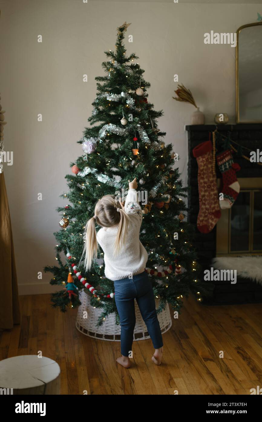 Blick von hinten auf ein Kleinkind, das hoch oben auf den Weihnachtsbaum ragt Stockfoto