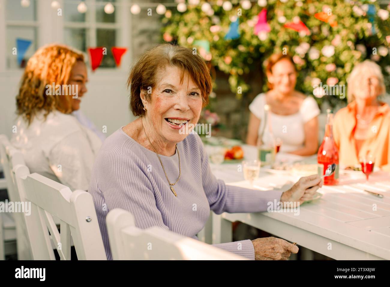 Porträt einer glücklichen Seniorin, die am Esstisch im Hinterhof sitzt Stockfoto