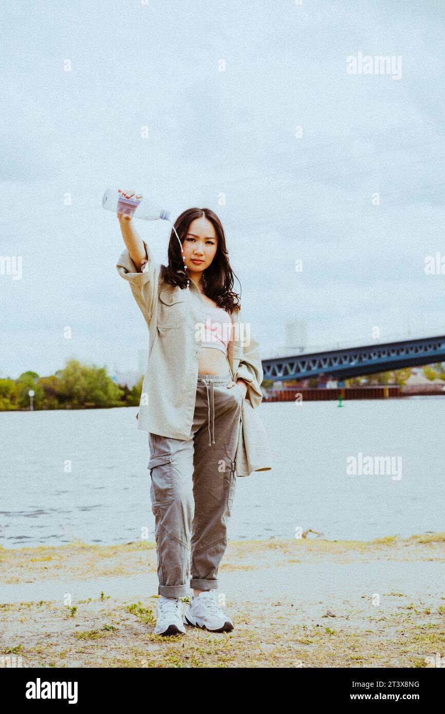 Porträt einer selbstbewussten jungen Frau, die Wasser aus der Flasche gegen den Himmel gießt Stockfoto