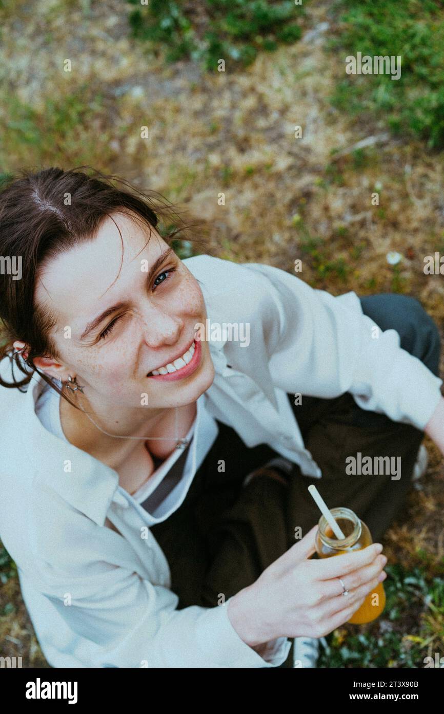 Hochwinkelporträt eines lächelnden jungen nicht-binären Menschen, der Saftflasche hält Stockfoto