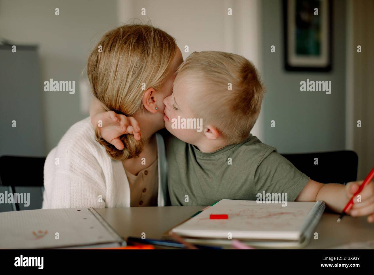 Junge mit Down-Syndrom, der Schwester küsst, während er am Esstisch sitzt Stockfoto
