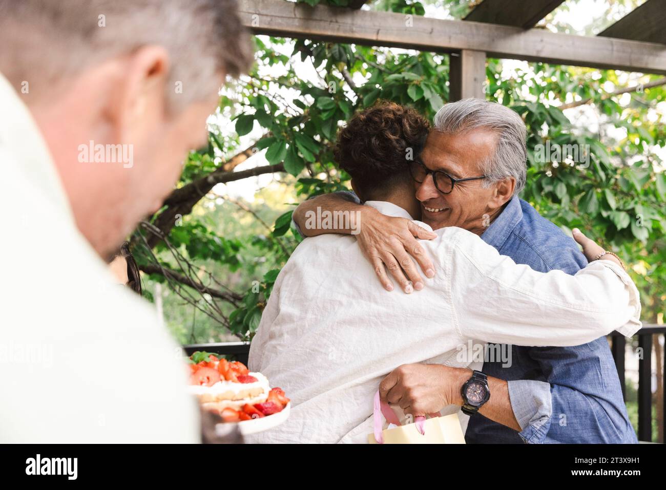 Glücklicher Senior-Mann, der den jungen Mann auf der Dinnerparty umarmt Stockfoto