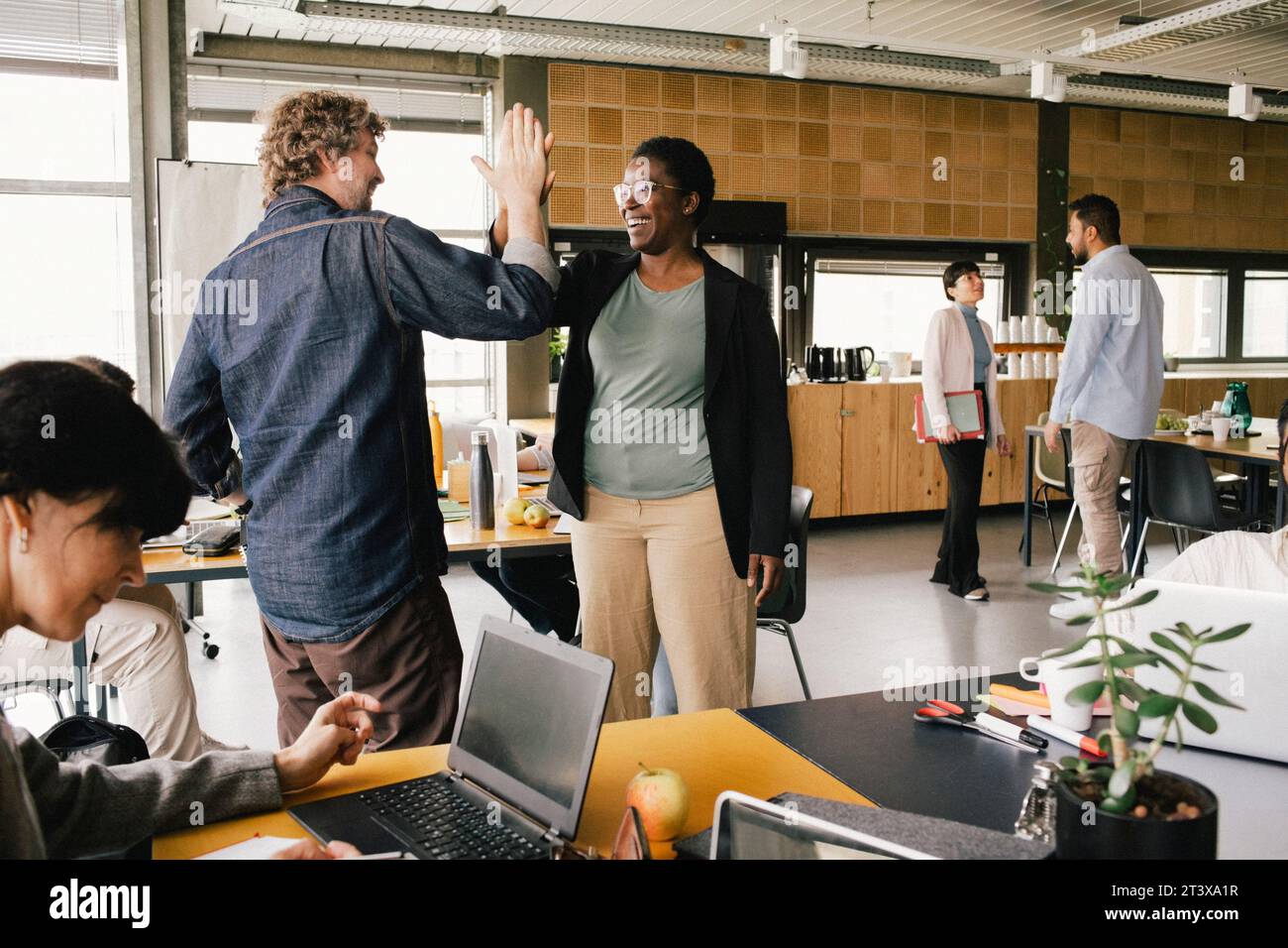 Glückliche Geschäftsfrau, die einem Kollegen im Büro High-Five gibt Stockfoto