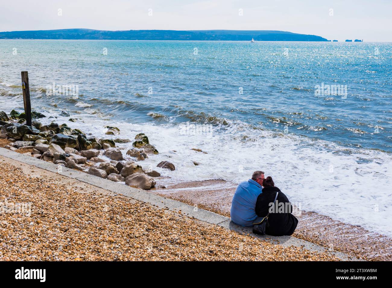 Ein Paar sitzt am Meer, die Needles und der Rest der nordwestlichen Isle of Wight im Hintergrund. Milford on Sea, New Forest, Hampshire, Engl Stockfoto