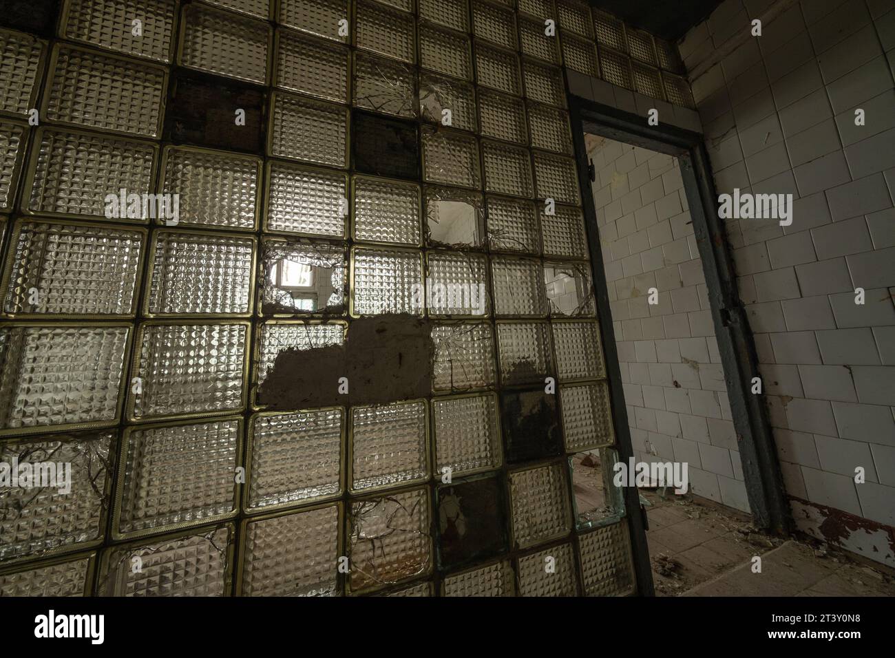 Von oben über der Tür mit gebrochenen Gläsern Metallstabtrennwand in Zementmauergebäude mit ungesäuertem, verstreuten Müllboden bei Tageslicht Stockfoto