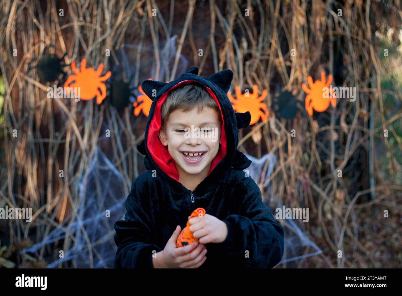 Frohes Halloween. Porträt des glücklichen Vorschuljungen im schwarzen Drachen-Faschingskostüm. Kind hat Spaß, Ballon aufblasen. Halloween-Party im Freien, Herbst Stockfoto